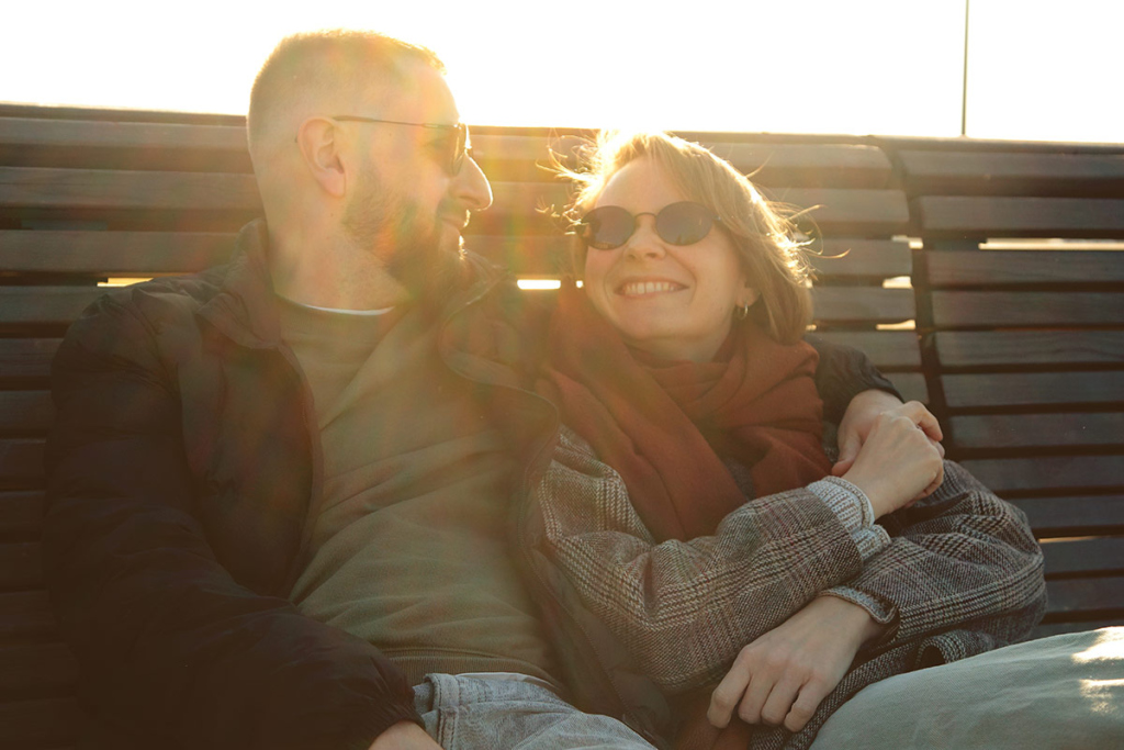 Молодые мужчина и женщина сидят обнявшись на скамейке 