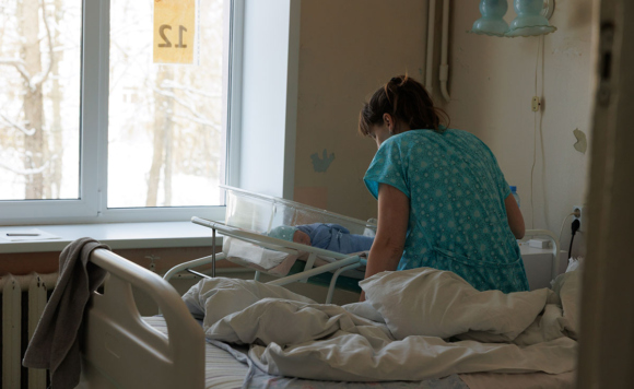 С новорождённым ребенком - 38-летняя Екатерина, третий сын Даниил. Женщина в палате роддома склонилась над кювезом младенца