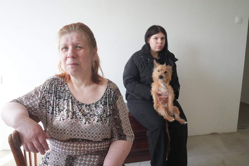 Женщина среднего возраста и ее дочь с собачкой на фоне стены в квартире