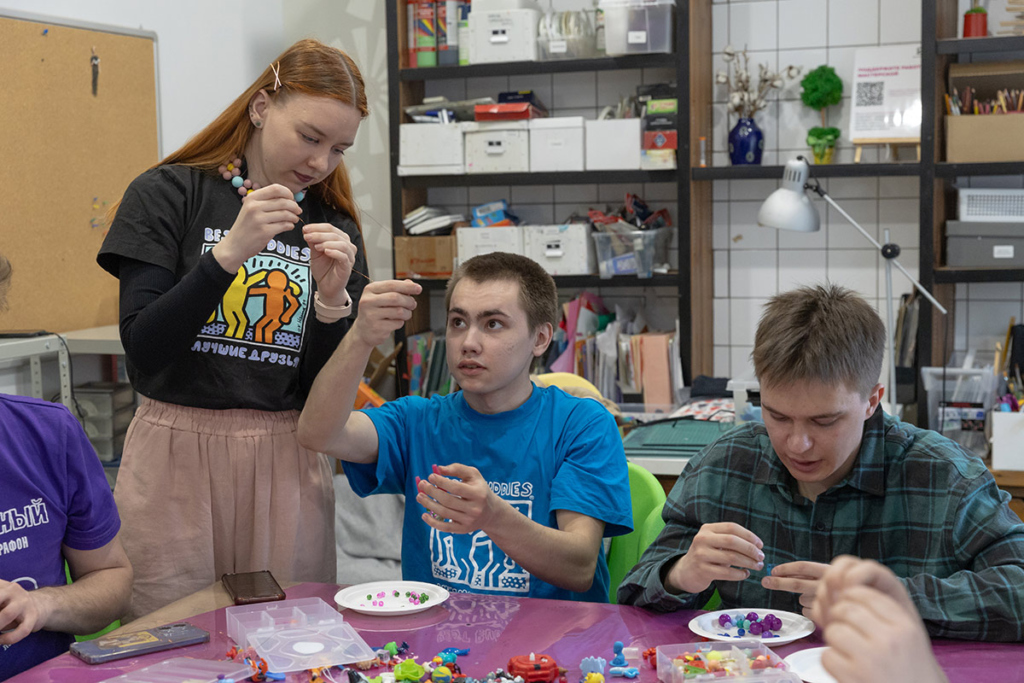 Волонтеры и подопечные. Девушка и два парня занимаются рукоделием