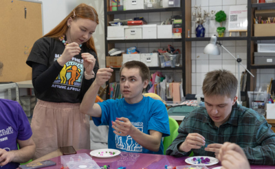 Волонтеры и подопечные. Девушка и два парня занимаются рукоделием