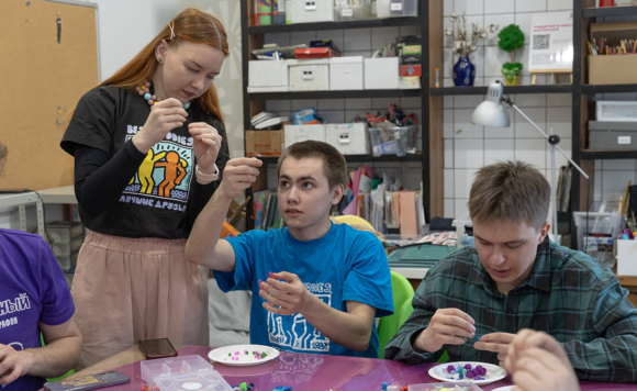 Волонтеры и подопечные. Девушка и два парня занимаются рукоделием