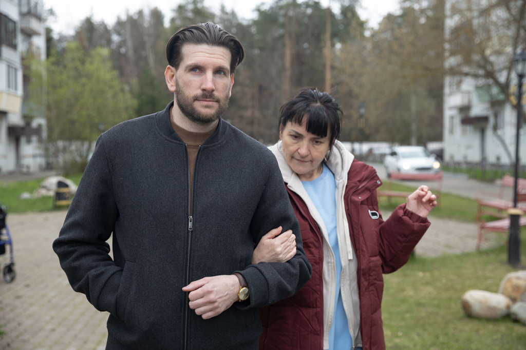 Молодой мужчина ведет под руку взрослую женщину