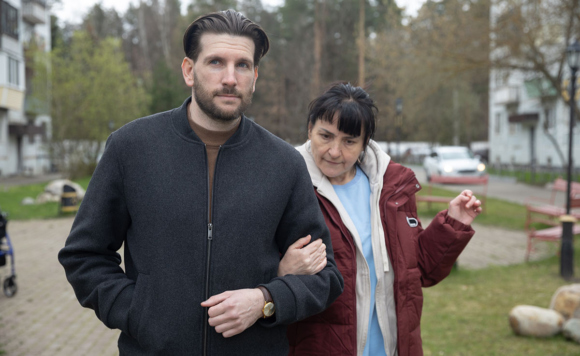 Молодой мужчина ведет под руку взрослую женщину