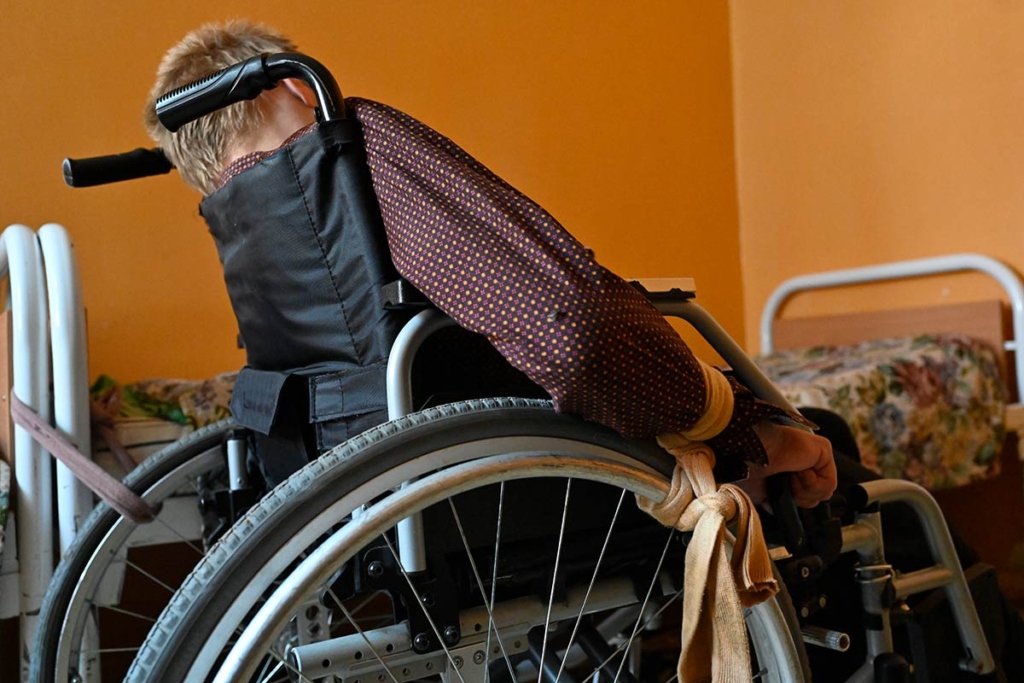 двойная фиксация. Этот человек мог бы передвигаться на кресле. Но кресло привязано к кровати. А руки привязаны к колесам. Чтобы не крутил.