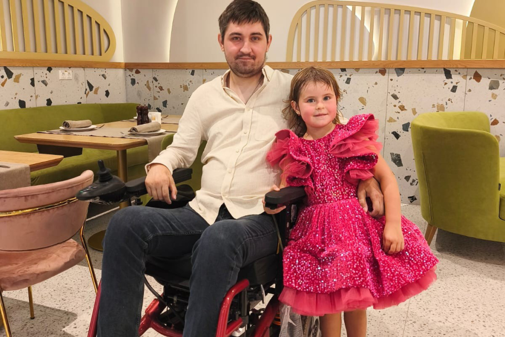 Мужчина на инвалидной коляске с маленькой дочкой